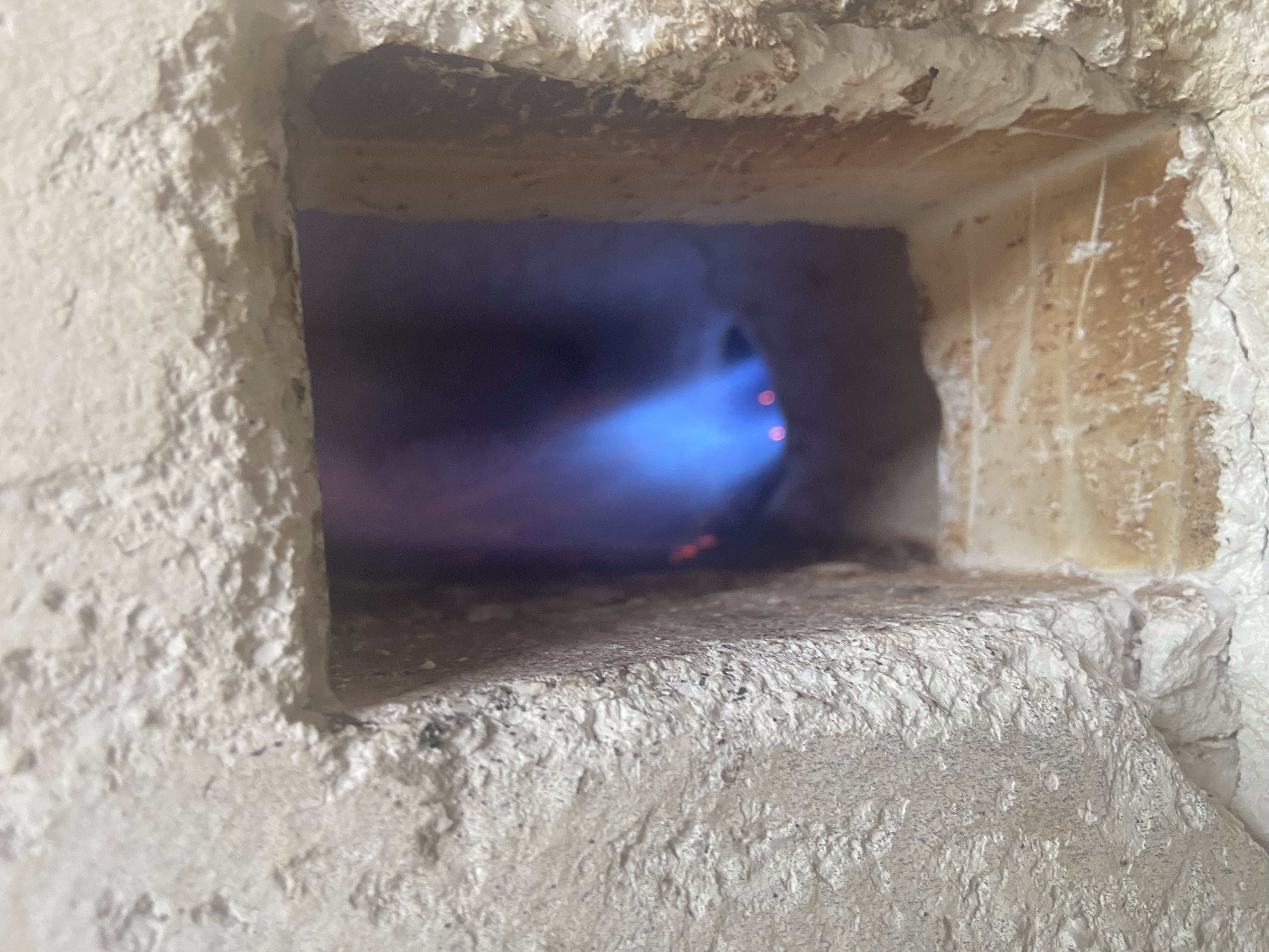 Looking into the forge chamber — blue propane flame glowing inside the refractory lining