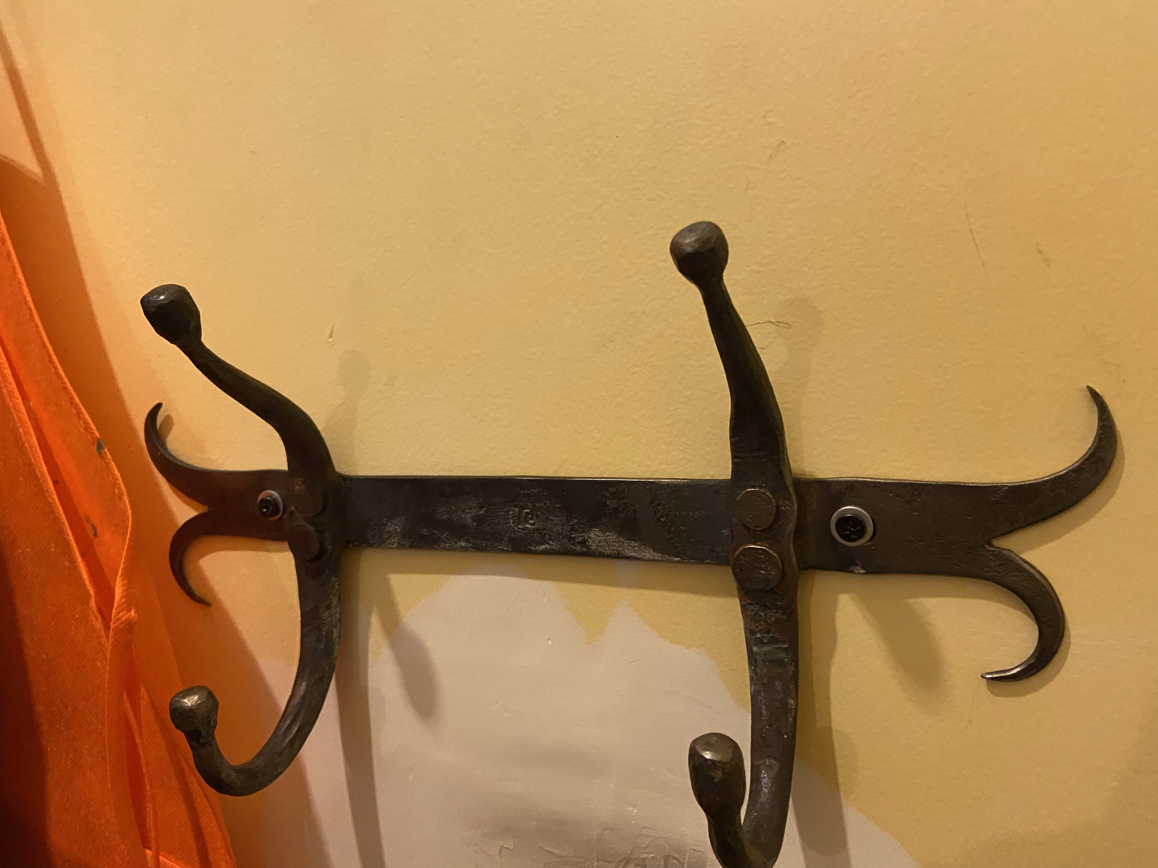 Three-hook forged iron coat rack mounted to a wall — scrolled hook ends, punched backplate