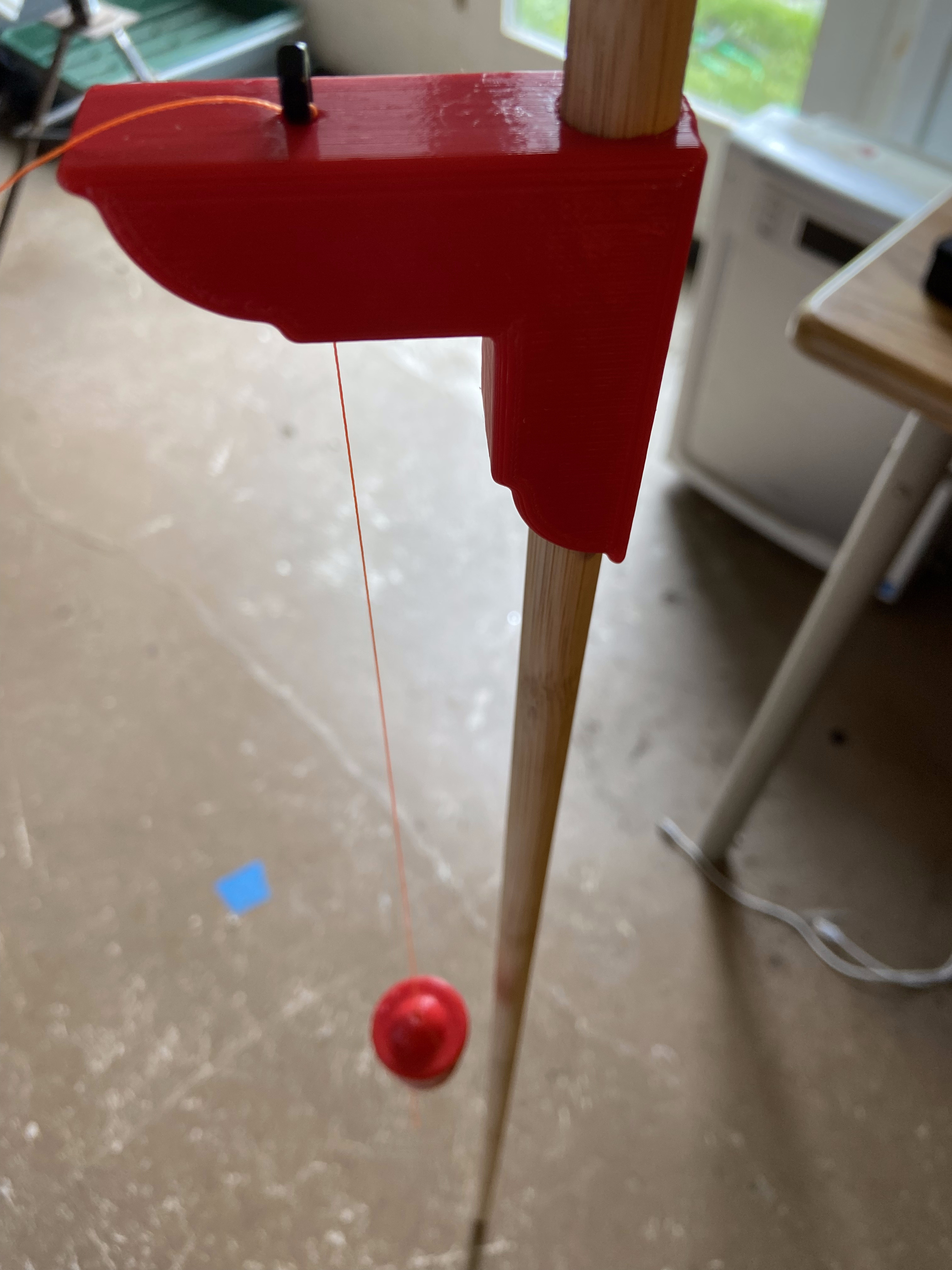 Gnomon apparatus: vertical wooden rod with red 3D-printed right-angle bracket and plumb bob hanging from string