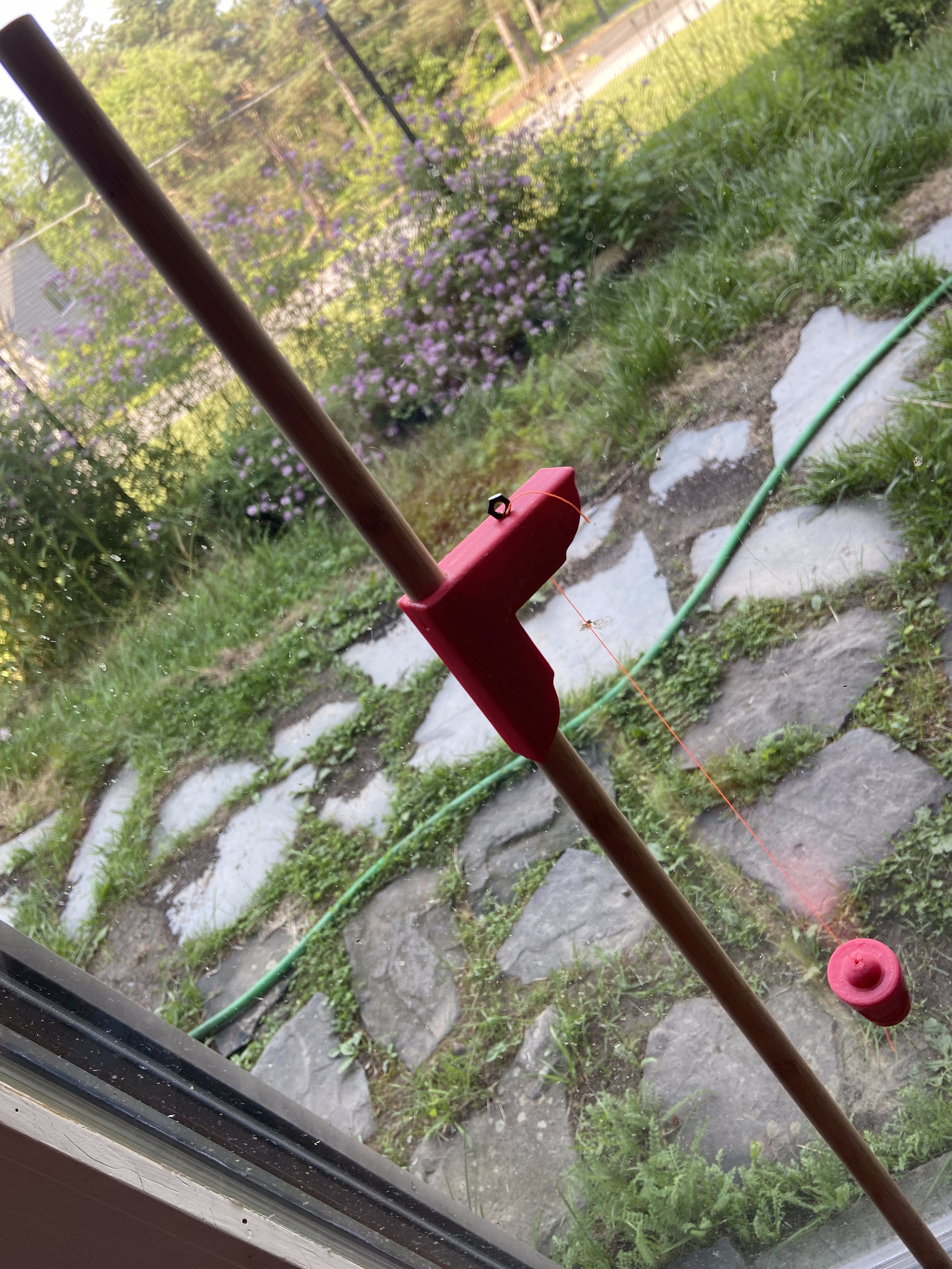 Gnomon rod and bracket deployed at a window with garden beyond — plumb bob ensuring vertical alignment