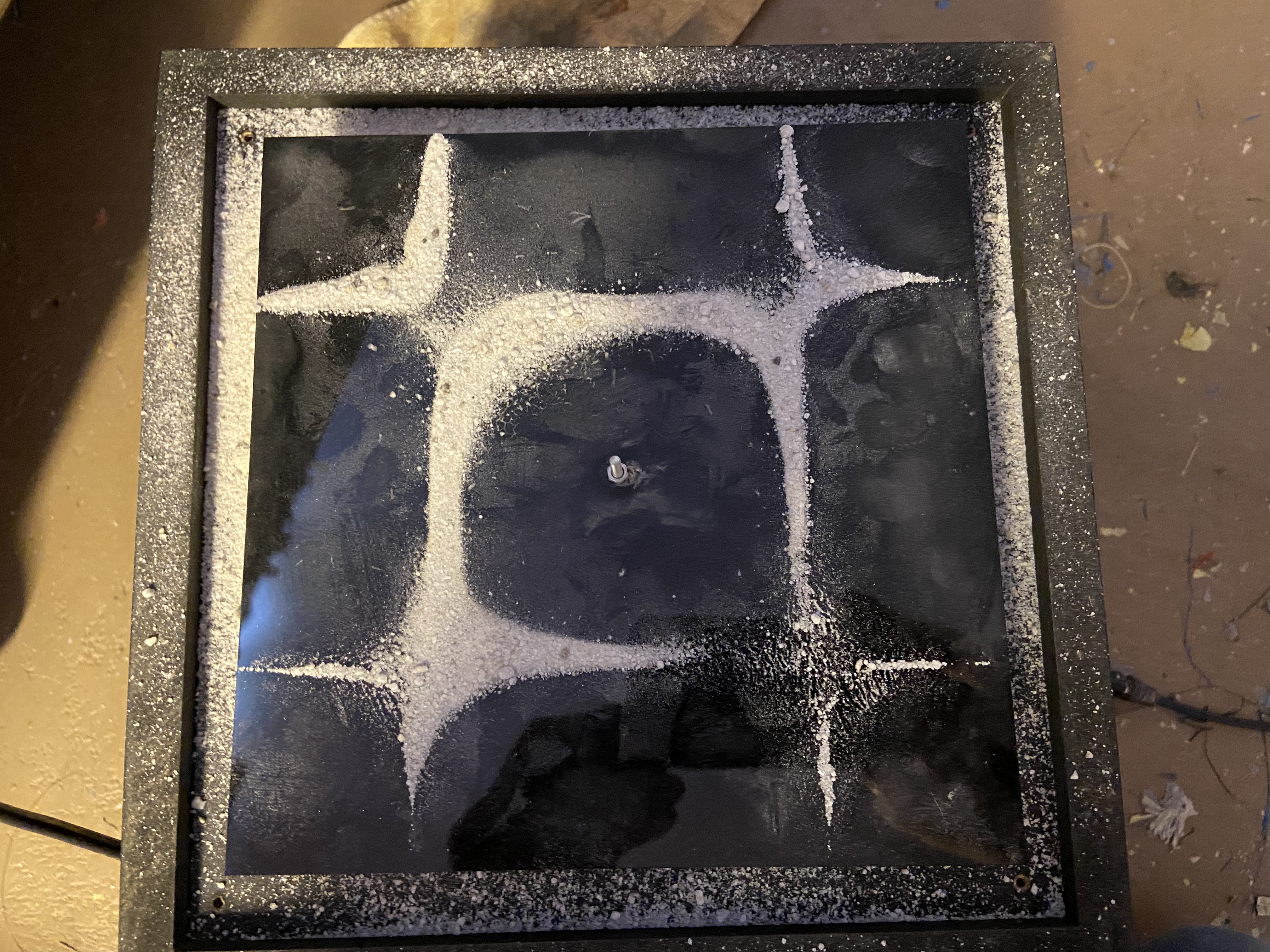 Four-pointed star Chladni figure in white sand on black plate — crisp and dramatic