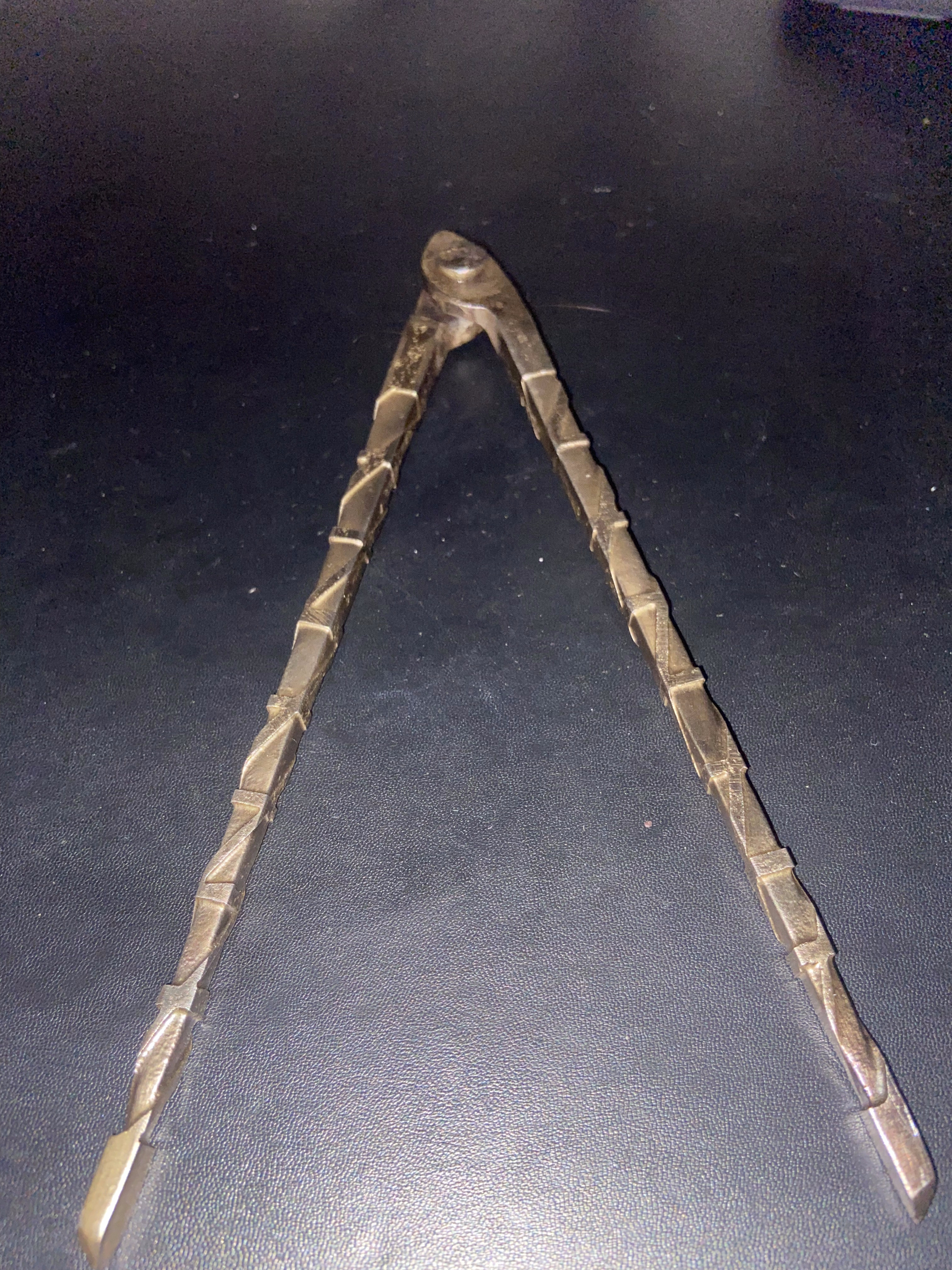 Forged steel tongs open in a V-shape, handles showing etched faceted texture