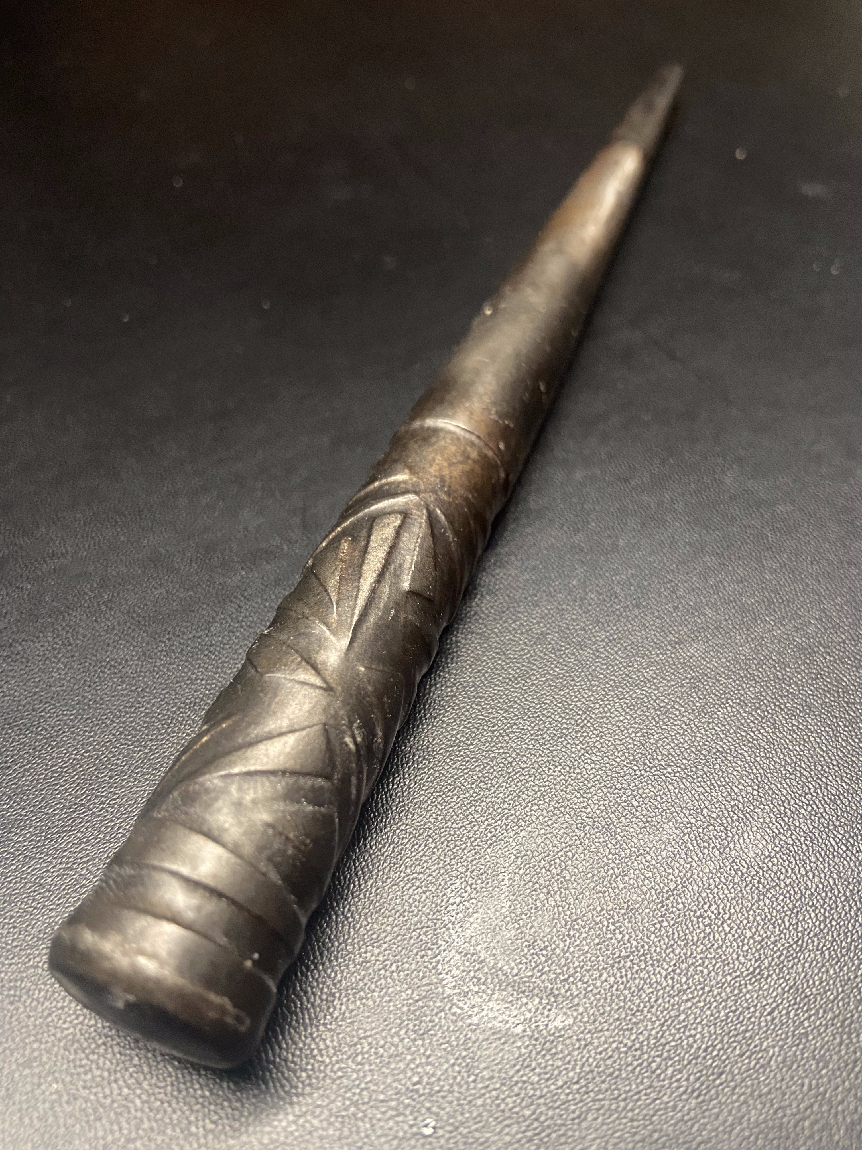 Tapered forged steel wand with etched spiral surface detail on dark background