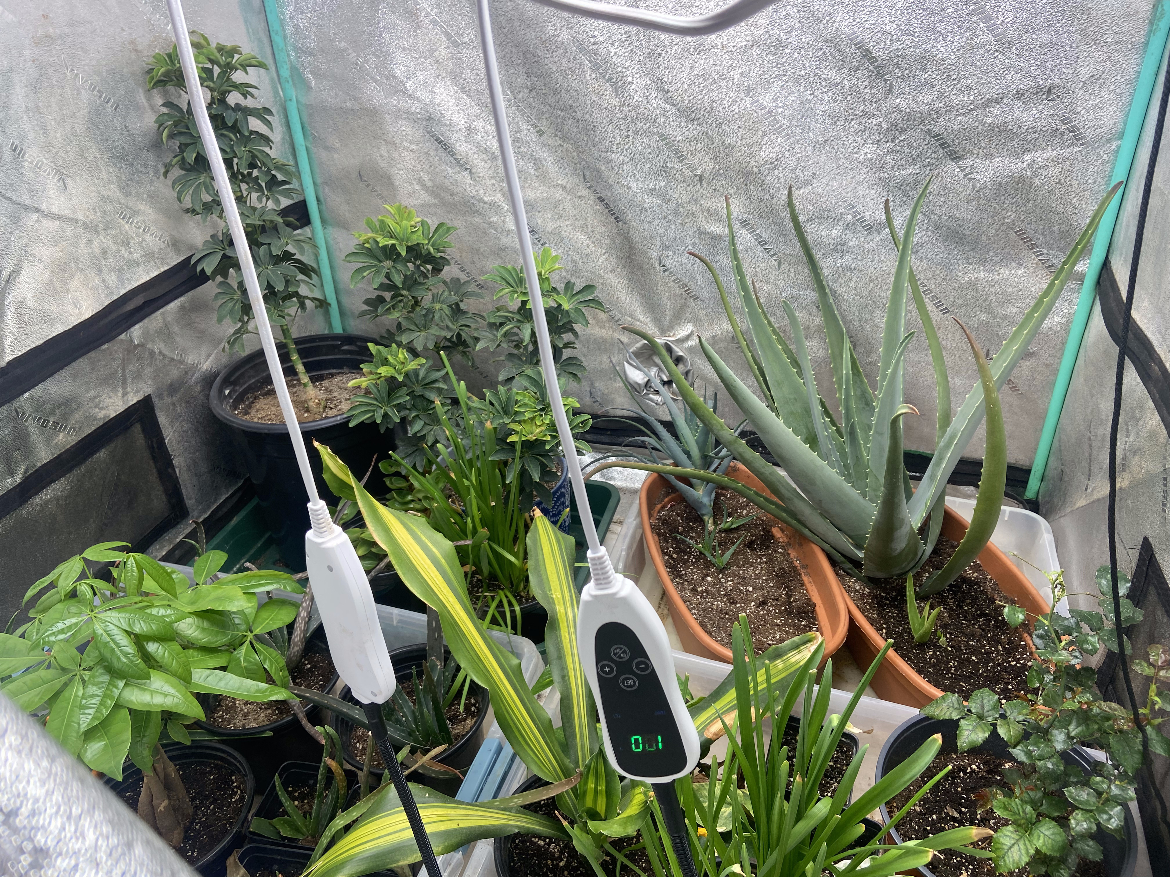 Grow tent interior showing multiple plants with soil moisture sensor probes and digital readout display