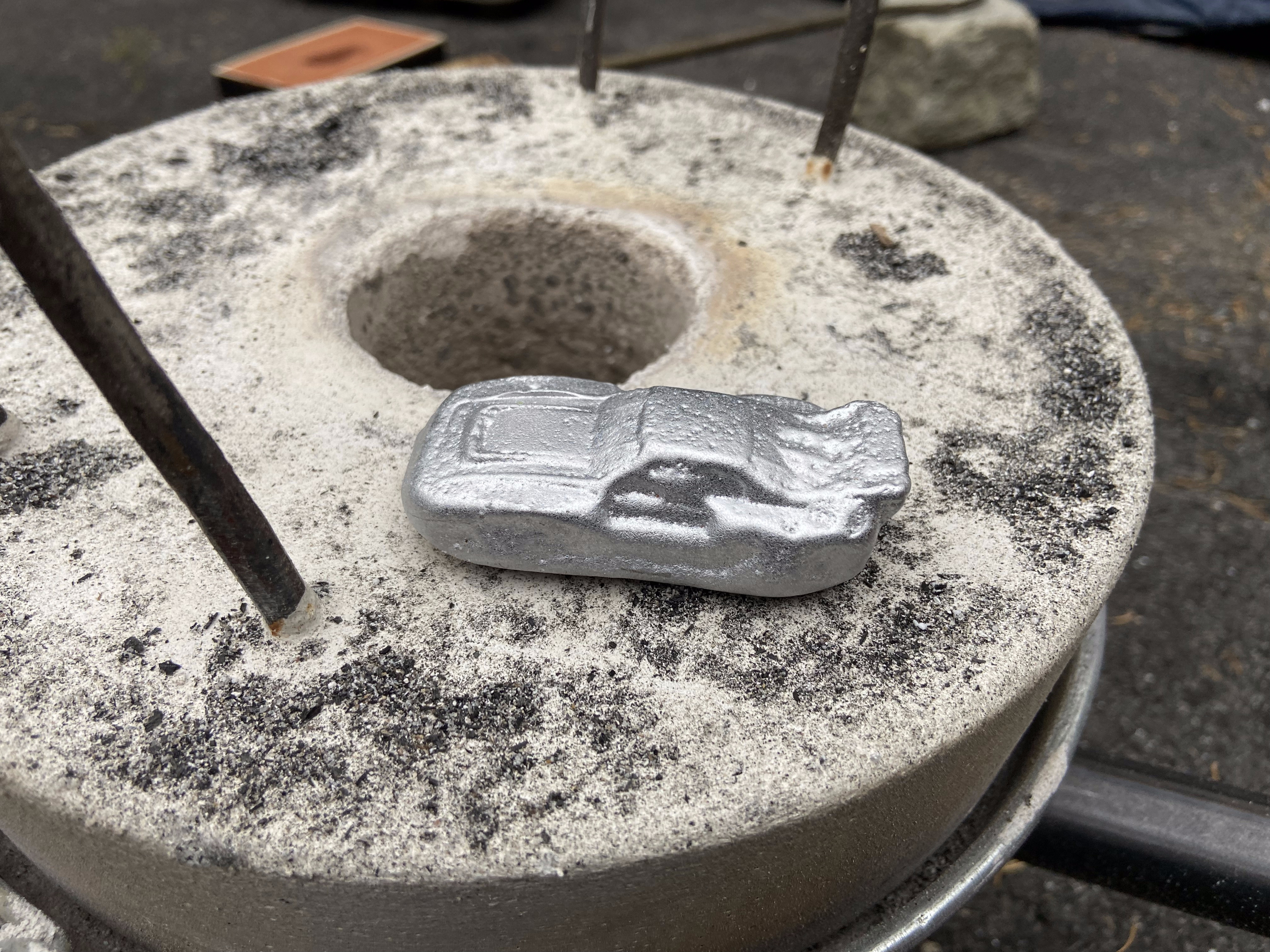 Cast aluminum toy car sitting on the furnace lid, still dusted with sand